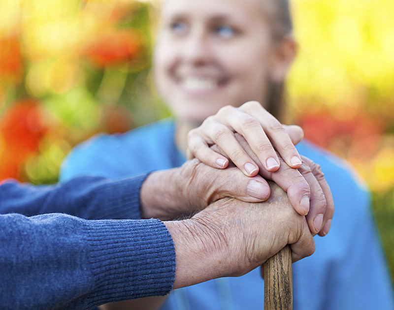 Caregiver with her hadns on top of elderly man's hands